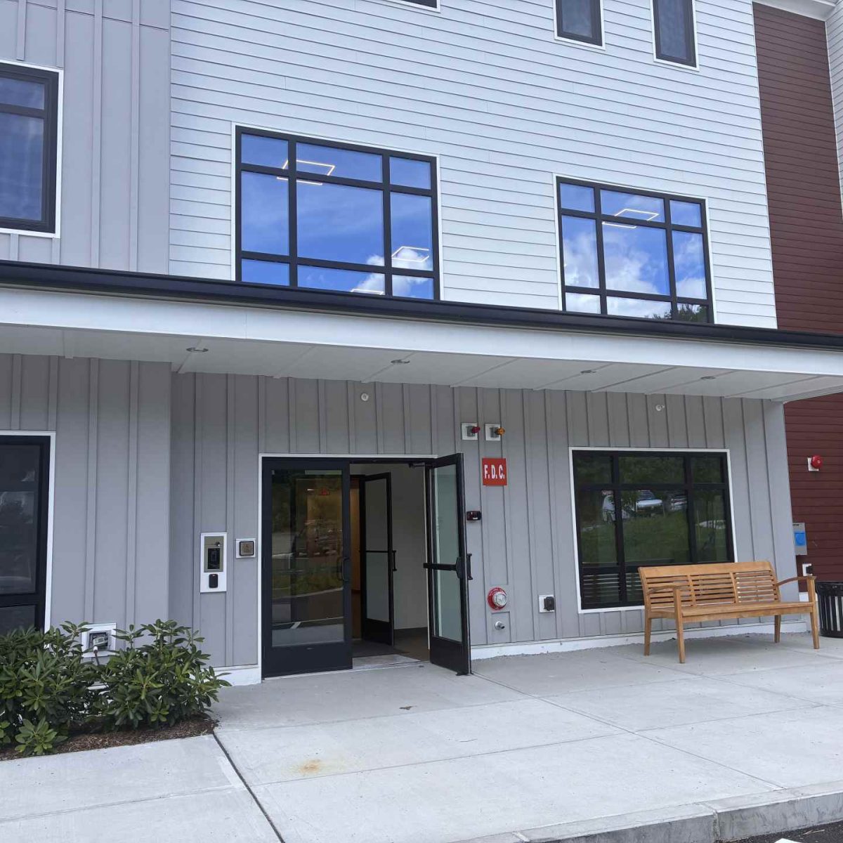 Entrance to McManus Manor senior apartments with open glass doors, covered walkway, and a bench outside