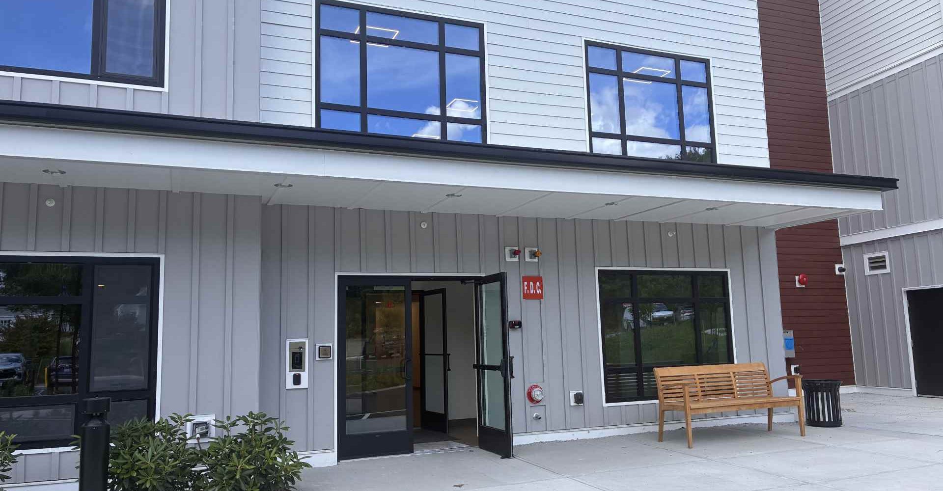 Entrance to McManus Manor senior apartments with open glass doors, covered walkway, and a bench outside