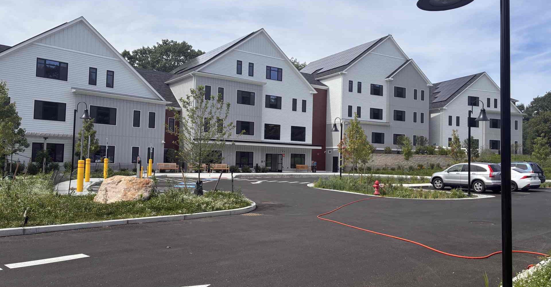 Multiple gabled apartment buildings at McManus Manor senior apartments with solar panels, a paved driveway, and landscaped grounds