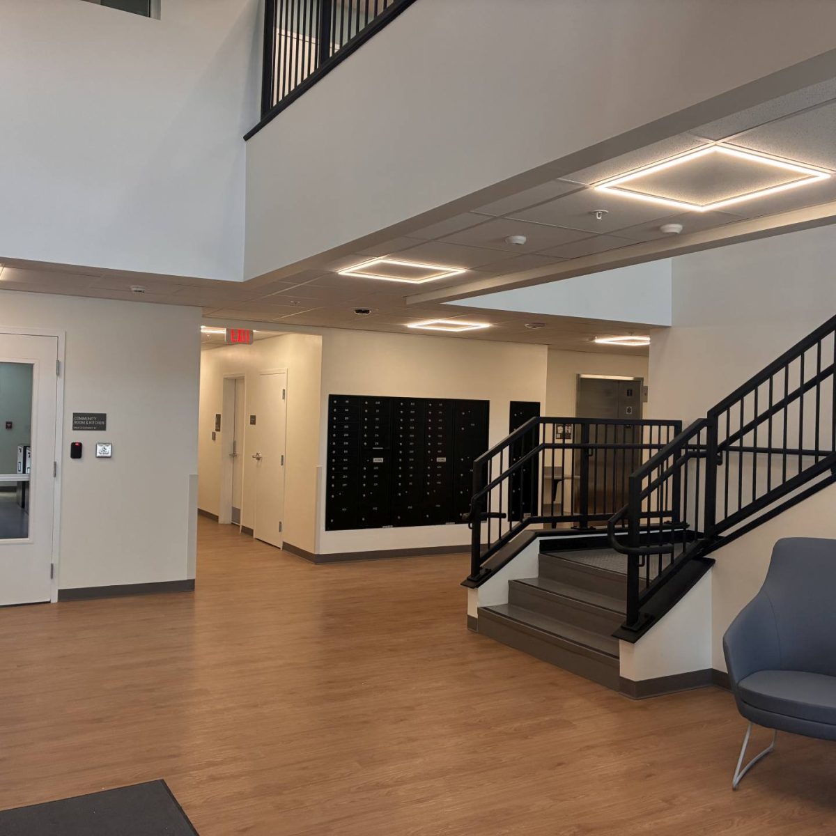 Building lobby with wood-look flooring, mailboxes, a staircase with black railings, and seating area near the entrance.
