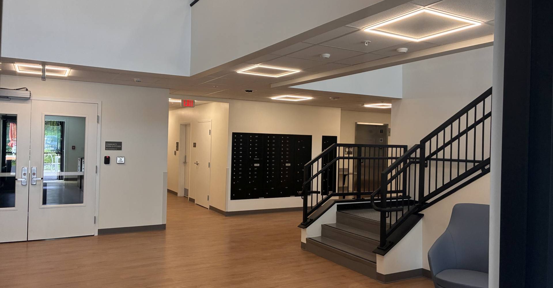 Building lobby with wood-look flooring, mailboxes, a staircase with black railings, and seating area near the entrance.