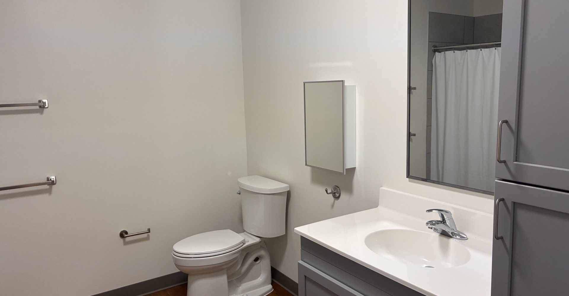 Bathroom in a senior apartment with toilet, vanity sink, mirrored medicine cabinet, and grab bars