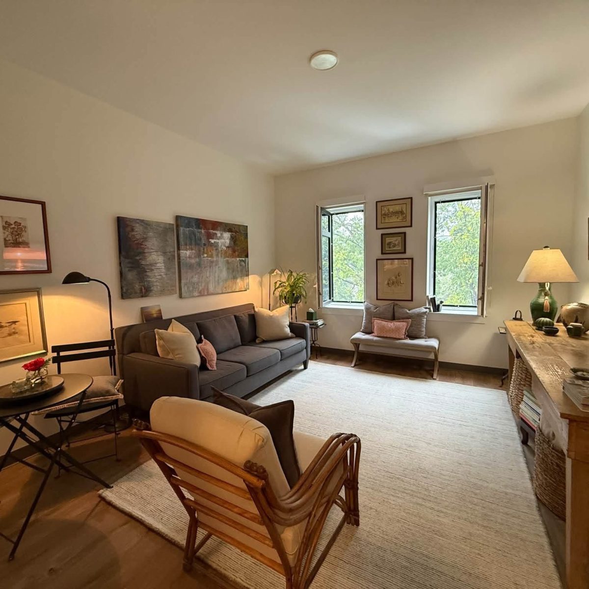 Cozy senior apartment living room with a sofa, armchairs, artwork, and large windows overlooking trees