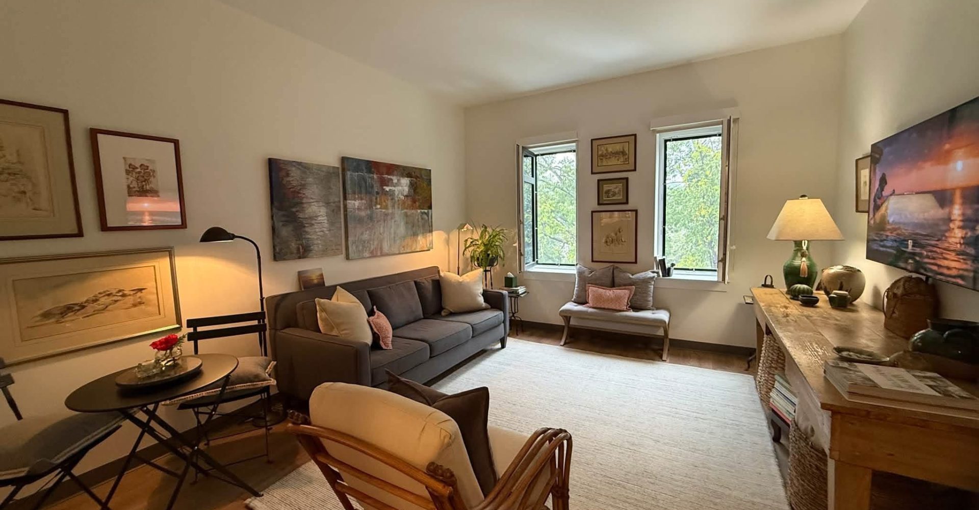 Cozy senior apartment living room with a sofa, armchairs, artwork, and large windows overlooking trees